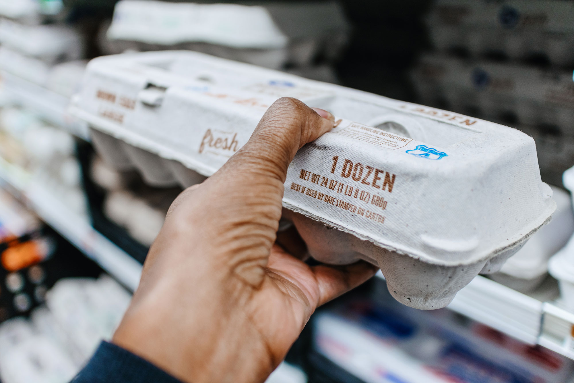 a customer picks up a carton of eggs at the grocery story